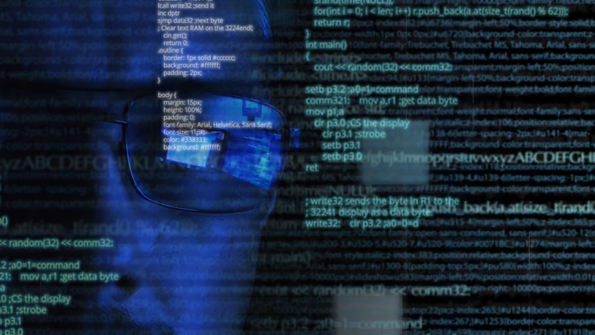 A person wearing a pair of glasses reflecting the image of two computer screens in blue light. Next to the face is a page of computer code.