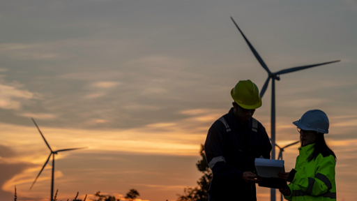 Two engineers working and holding the report at wind turbine farm
