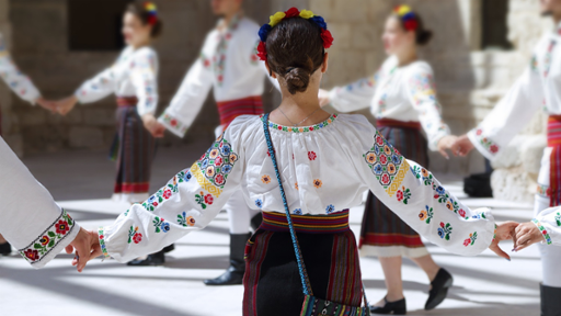 Female dancers wearing one of the traditional folk costumes from Romania dancing in a circle while holding hands