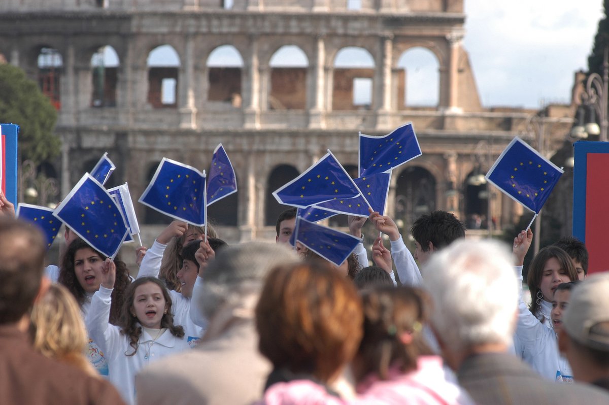 Photograph of schoolchildren waving small European Union flags in front of the Colosseum in Rome