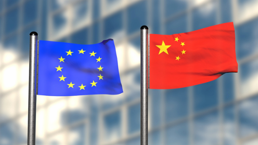 A Chinese flag next to a European Union flag on steel poles in front of a blurred glass skyscraper